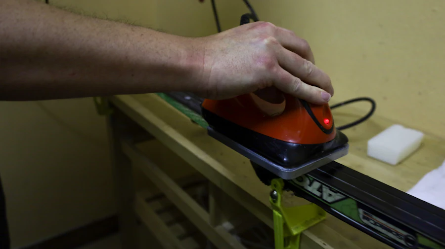 A hand running a red waxing iron along a ski clamped to a workbench.